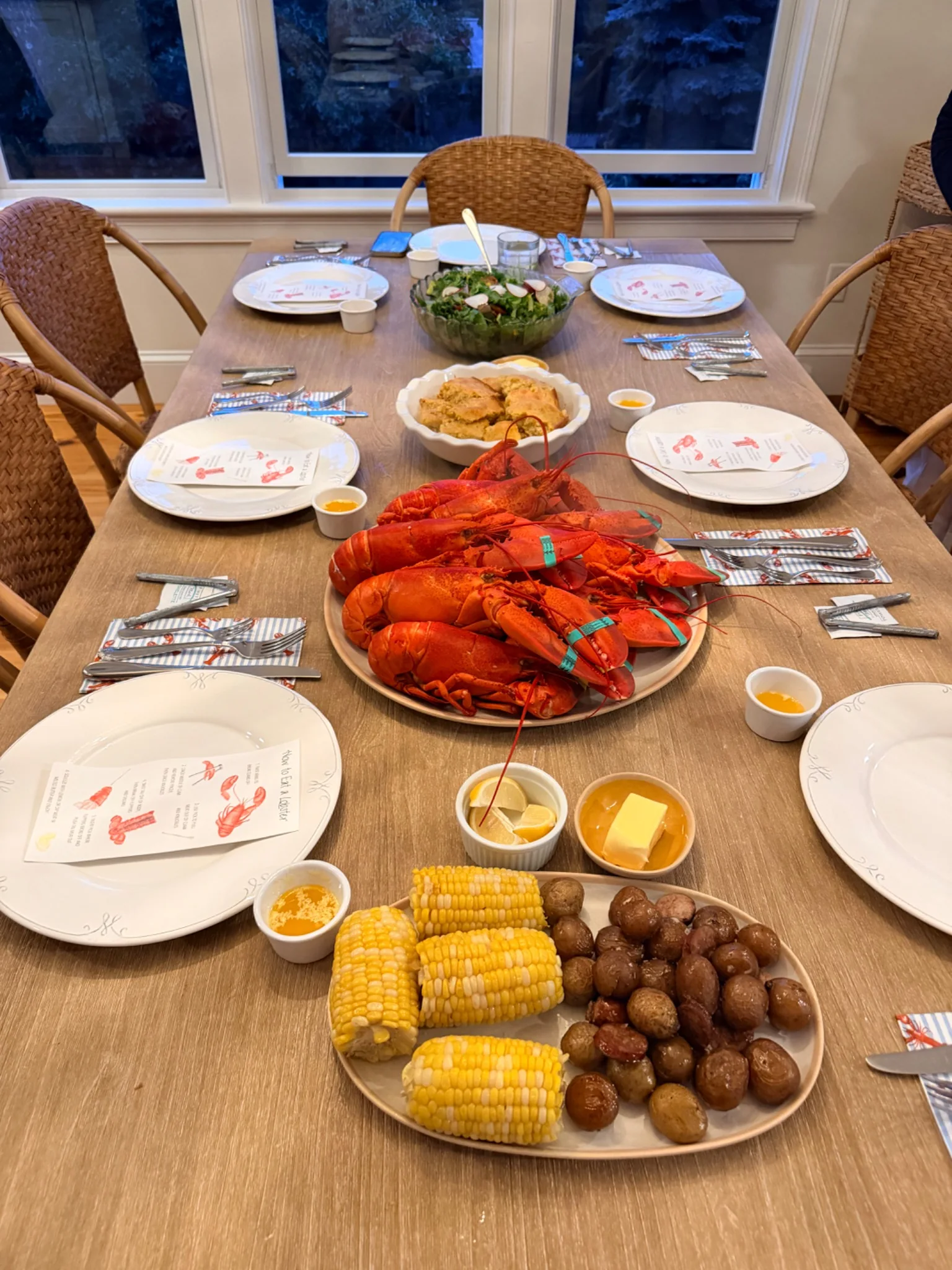 A New England clambake table prepared with lobster, corn, potatoes, salad, and place settings