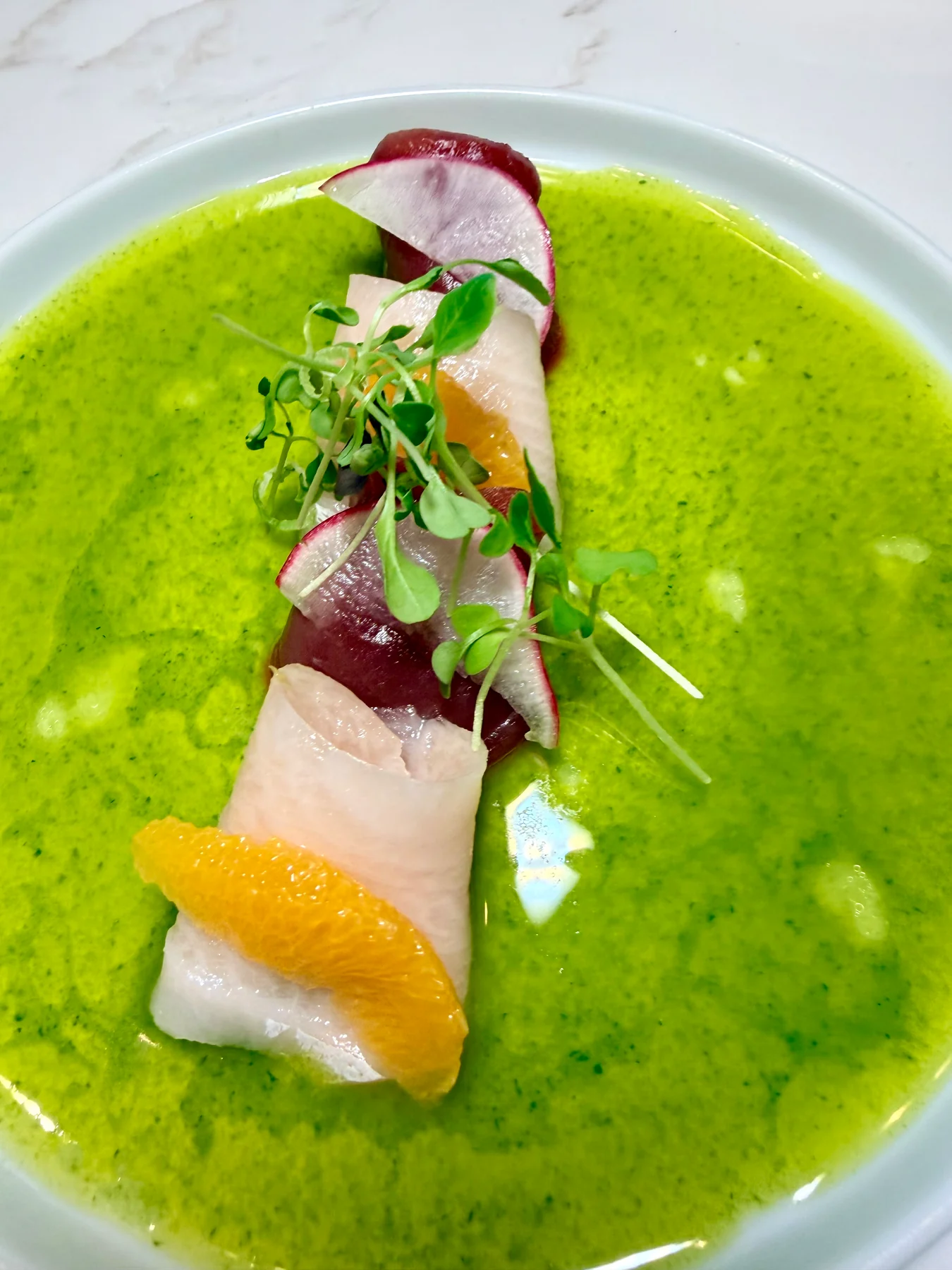 Thinly sliced seafood with citrus, radish, and microgreens in a bright green sauce